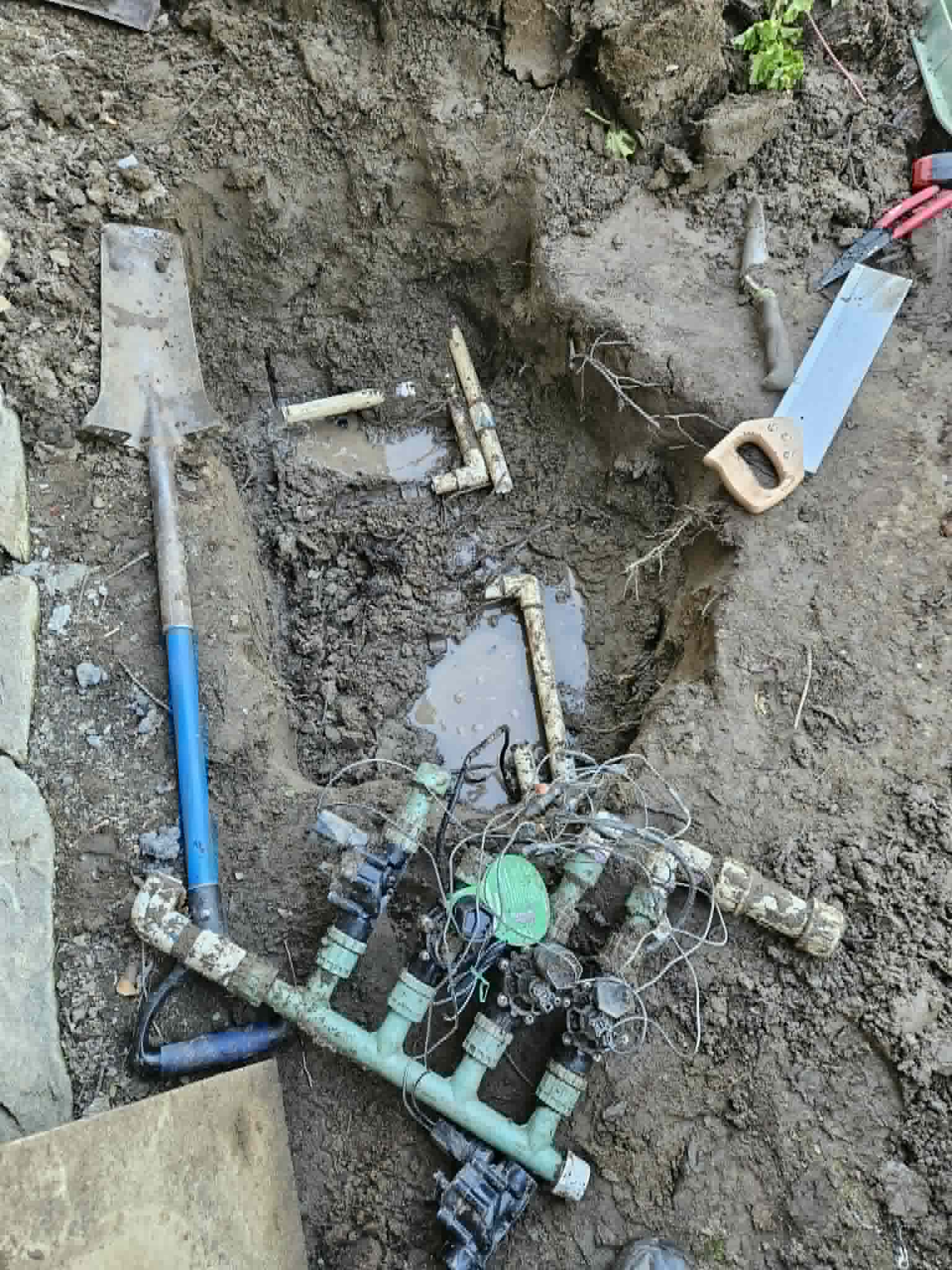 Step two of an irrigation manifold rebuild with the trench opened, tools nearby, and the valve assembly prepared for replacement